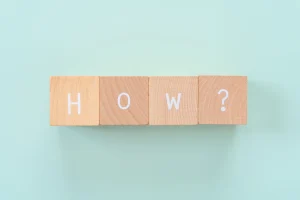 HOW？と書かれた積み木が青い背景の上にある