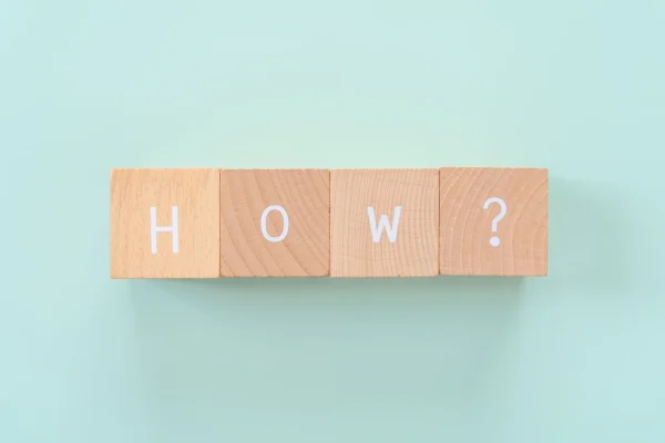 HOW？と書かれた積み木が青い背景の上にある