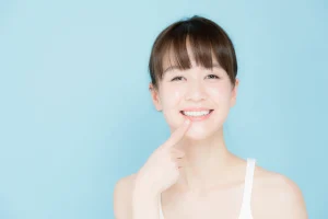白い歯を指さして笑う女性