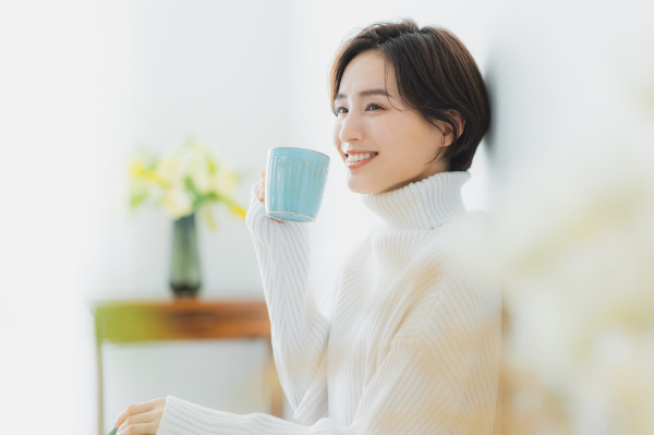 マグカップ片手にリラックスする白いニットを着た女性