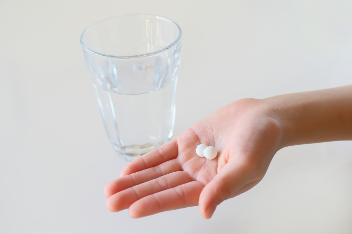 鎮痛剤をのせた手と水の入ったコップ
